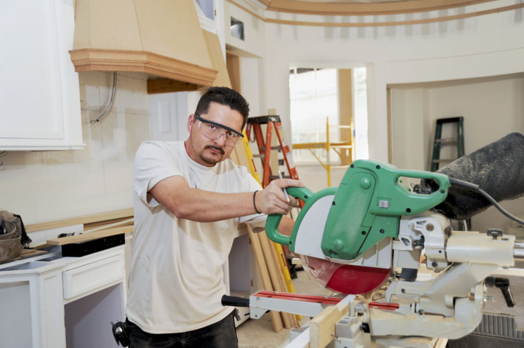 Carpenter uses a miter saw to cut molding for a custom kitchen remodel