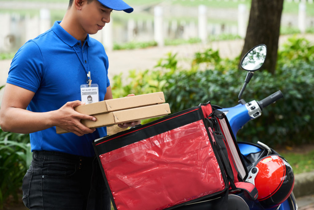 Pizza delivery driver holding pizza boxes next to his moped